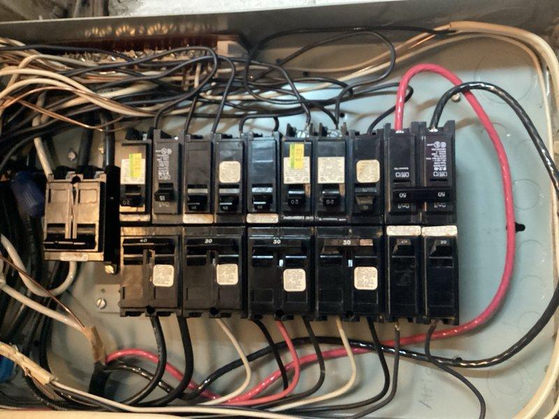 Conducted comprehensive electrical panel assessment in basement area to provide estimate for new or additional panel installation. Inspected existing electrical panel, documenting current configuration with approximately 10-12 circuit breakers arranged in dual rows on metal backing plate. Evaluated wire organization, noting congested conductor routing at panel top with multiple tan, black, and red wires. Assessed panel capacity, breaker arrangement, and overall system condition to determine requirements for panel upgrade or secondary panel addition. Photographed existing electrical infrastructure and surrounding installation area to develop accurate scope of work and material specifications for proposed panel installation.