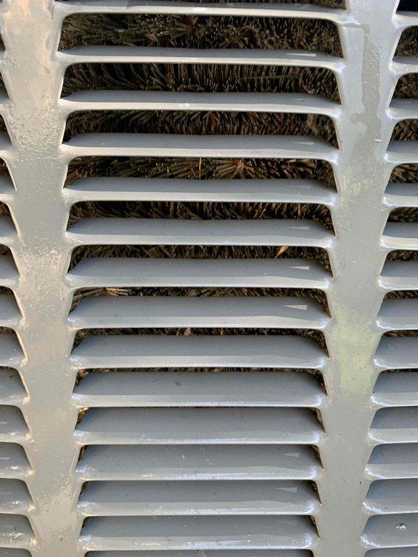 # HVAC Cooling System Maintenance Completed

Performed comprehensive cooling maintenance tune-up on a 10-year-old air conditioning system. System operational status confirmed throughout service visit.

## Work Performed

**Air Filter Service:**
Inspected air filter and documented significant dust and debris accumulation across pleated filter media. Filter showed considerable particulate buildup with dark gray to black discoloration throughout pleated surfaces, indicating extended use period. Uneven dust distribution patterns observed across filter face, suggesting varied airflow characteristics. Wire mesh grid intact with no structural damage noted.

**Exterior Ventilation Inspection:**
Examined outdoor unit ventilation grille and identified substantial organic debris accumulation. White-painted louvered grille housing dried leaves, twigs, and compacted plant matter behind horizontal slats. Debris appeared dried and matted, indicating prolonged accumulation period. Material obstruction