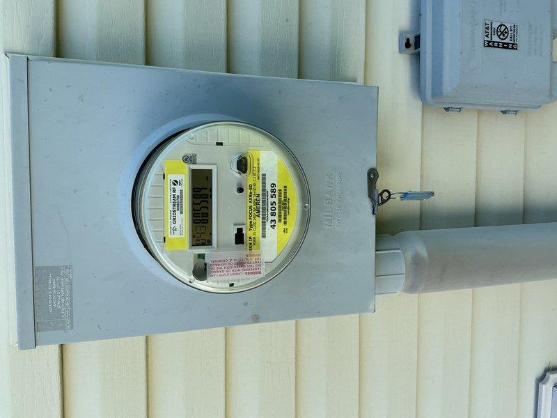 Completed electrical fixture installation including installation of new electrical outlet with standard duplex receptacle and cover plate on interior wall. Installed exterior electrical meter enclosure with digital electric meter, junction box, and associated conduit runs with proper mounting hardware and securing straps on building exterior siding. All components installed to code specifications with proper grounding and weatherproofing measures for exterior installations.