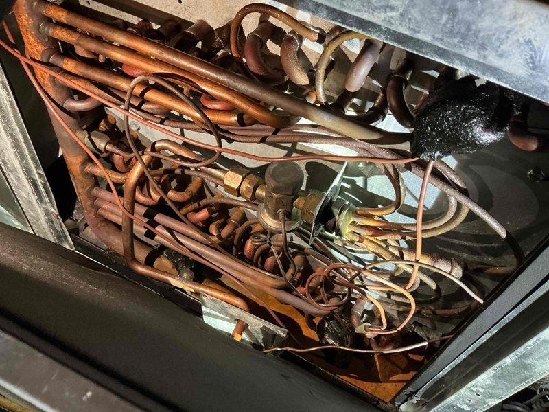 Responded to no cooling call on second floor Unico system. Upon arrival, learned unit had been frozen the previous day and was turned off. Accessed attic space via pull-down stairs to inspect system. Found evaporator coil with visible copper tubing and heat exchanger assembly. Coil showed signs of oxidation and discoloration on copper lines, with brass valve and fittings present. Inspected flexible aluminum ductwork routed through attic joists and spray foam insulation areas. System had been shut down allowing coil to thaw. Documented equipment condition with photos showing coil assembly and attic installation layout for service records.