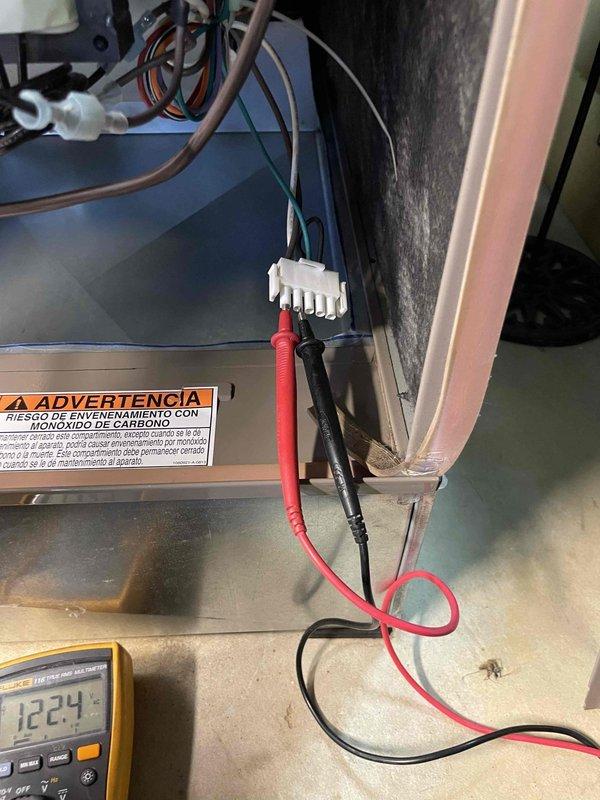 Responded to no-cool complaint on 10-year-old York AC unit with no airflow and condensation on suction line. Upon arrival, found unit completely inoperative with no fan operation. Performed electrical diagnostics using Fluke multimeter to test control circuit voltage at electrical connections. Measured 12.24 volts at control board wiring harness to verify power supply and diagnose control circuit failure. Identified failed component preventing unit operation and causing system shutdown.