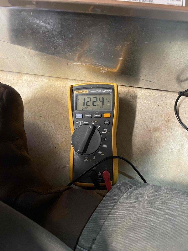 Responded to no-cool complaint on 10-year-old York AC unit with no airflow and condensation on suction line. Upon arrival, found unit completely inoperative with no fan operation. Performed electrical diagnostics using Fluke multimeter to test control circuit voltage at electrical connections. Measured 12.24 volts at control board wiring harness to verify power supply and diagnose control circuit failure. Identified failed component preventing unit operation and causing system shutdown.