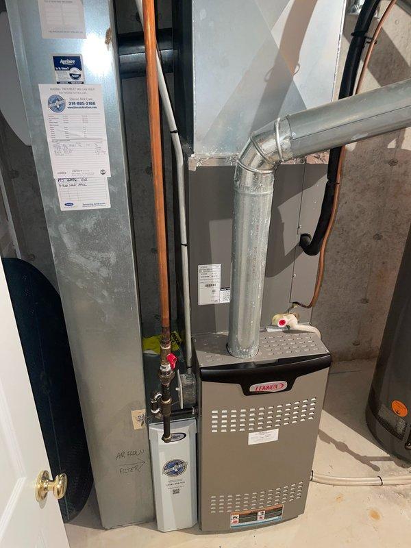 Responded to service call for residential AC system unable to cool below 75 degrees and continuously running. Upon arrival, performed diagnostic inspection of 10-year-old outdoor condensing unit located at side of home and indoor Lennox furnace/air handler system. Inspected air filter condition, verified proper airflow through pleated media filter, and checked refrigerant lines and ductwork connections. Documented existing equipment configuration including furnace unit, water heater proximity, and copper refrigerant line routing for service records.