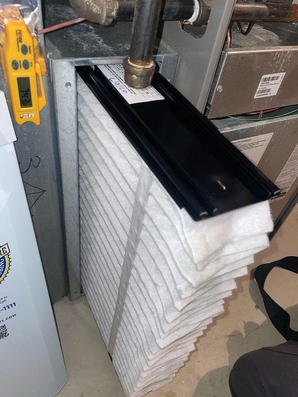 Responded to service call for residential AC system unable to cool below 75 degrees and continuously running. Upon arrival, performed diagnostic inspection of 10-year-old outdoor condensing unit located at side of home and indoor Lennox furnace/air handler system. Inspected air filter condition, verified proper airflow through pleated media filter, and checked refrigerant lines and ductwork connections. Documented existing equipment configuration including furnace unit, water heater proximity, and copper refrigerant line routing for service records.