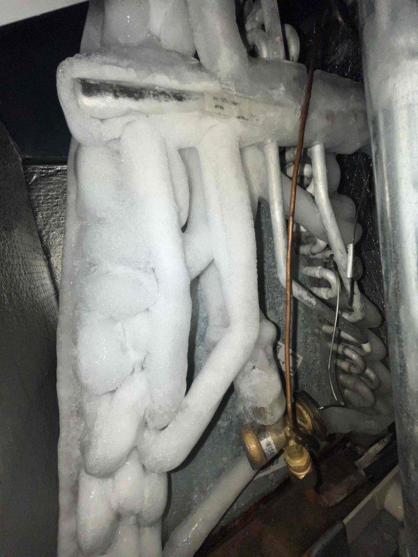 Responded to no cooling complaint on residential air conditioning system less than 10 years old. Upon arrival, found evaporator coil completely frozen with heavy ice buildup on refrigerant lines and coil surfaces. Advised customer to shut off unit and run fan only to allow ice to thaw. Identified severe frost accumulation on copper refrigerant lines and evaporator coil assembly indicating restricted airflow or possible low refrigerant charge. System requires follow-up diagnostic once ice has melted to determine root cause, which may include dirty air filter, blocked return air, failed blower motor, low refrigerant due to leak, or malfunctioning metering device.