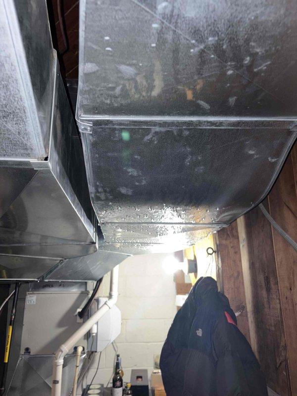 Responded to service call for condensation issue on flue liner at property with three HVAC units, all approximately four years old. Upon arrival, performed diagnostic assessment of the affected system using digital manifold gauges to check refrigerant pressures and system performance. Inspection revealed significant condensation accumulation on ductwork in mechanical space, with visible moisture patterns on the main supply plenum and surrounding components. Examined outdoor condensing unit and verified proper fan operation and airflow through coil assembly. Documented conditions with photos showing moisture buildup on interior ductwork and exterior unit configuration during testing. Identified condensation concern related to inadequate insulation or air sealing on cold surfaces in unconditioned space. Provided customer with findings and recommendations for addressing moisture infiltration to prevent ongoing condensation issues and potential water damage.