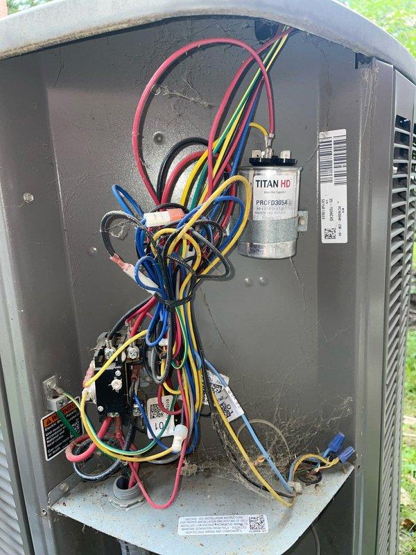 Responded to cooling complaint with unit unable to maintain setpoint, showing 9-degree temperature differential. Performed system diagnostic on residential split system with Lennox furnace and outdoor condensing unit. Inspected indoor air handler, ductwork, and outdoor unit components. Evaluated TITAN HD capacitor and electrical connections in condensing unit, noting wire routing and terminal conditions. Verified thermostat settings and system operation. Documented equipment condition with photos of indoor furnace installation and outdoor unit electrical compartment for service records.