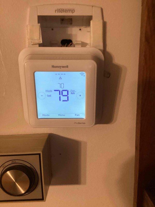 Responded to no cool call with thermostat displaying blank screen and no power. Upon arrival, found multiple thermostats installed on wall including non-functional Honeywell ProSeries unit. Diagnosed issue as loss of 24V power to thermostat from furnace control board. Inspected 10+ year old gray furnace unit located in ground-level utility area and verified proper voltage supply, traced wiring, and restored power to thermostat. System tested successfully with thermostat now displaying proper temperature readings and unit responding to cooling commands.