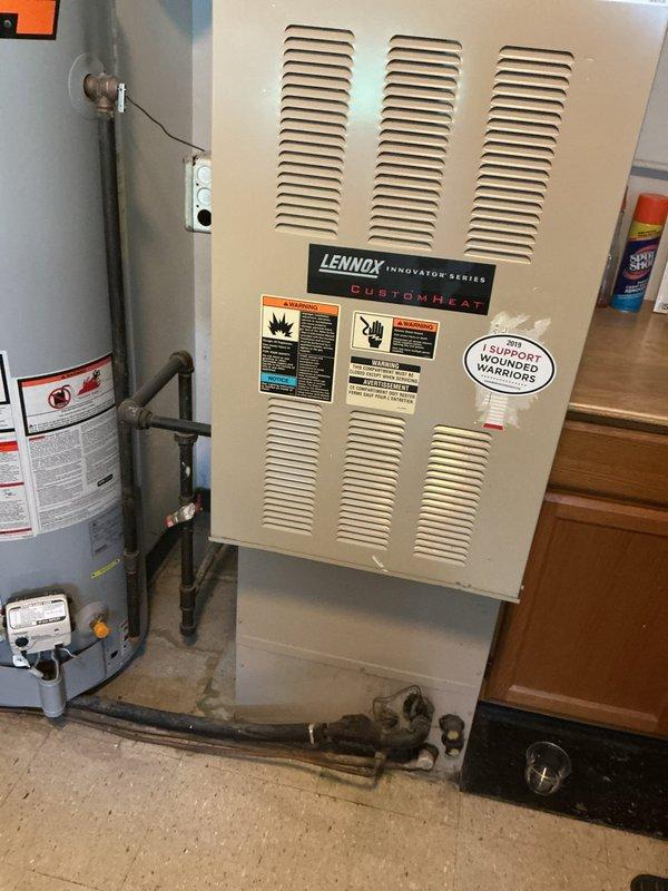 Responded to no cooling complaint on 10+ year old Lennox CustomHeat system located at rear of residence. Upon arrival, performed diagnostic evaluation of furnace and connected HVAC components. Inspected unit specifications, verified proper connections of refrigerant lines and condensate piping, and assessed overall system operation. Documented equipment condition with detailed photography of manufacturer labels, unit configuration, and installation setup including water heater integration. System evaluated and findings communicated to customer for resolution of cooling issue.