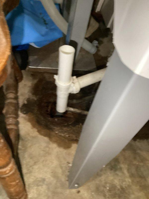 Responded to water leak reported at base of plumbing stack extending to drain line in basement utility area. Upon arrival, inspected PVC drainage system near HVAC equipment and water heater, identifying moisture on concrete floor beneath vertical stack and horizontal drain piping. Assessed T-junction configuration of drainage pipes, checked connections and fittings for signs of leakage or failure, and documented existing conditions of plumbing system and surrounding area for service records.