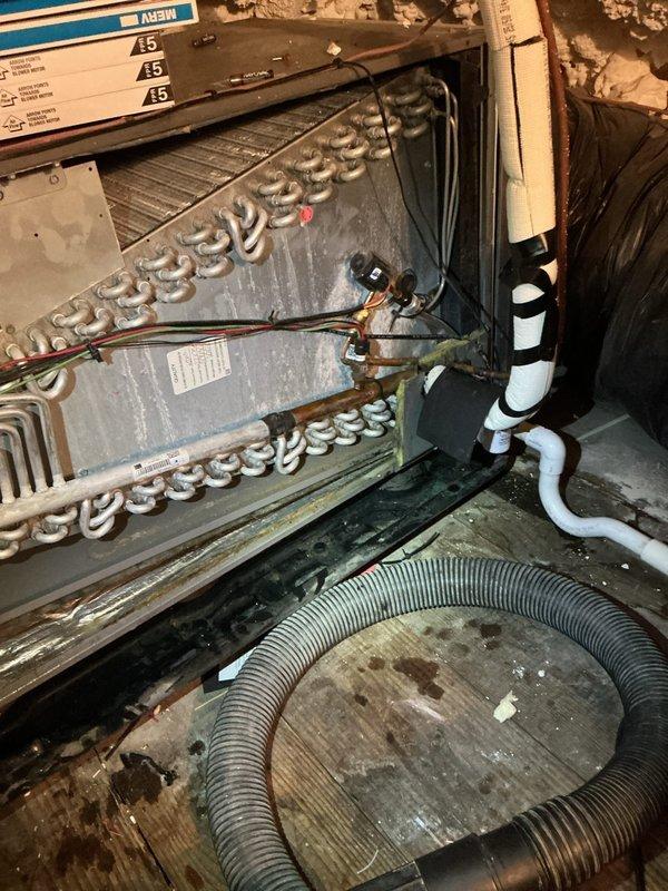 Responded to service call for attic-mounted air conditioning system experiencing refrigerant leak causing water damage to ceiling below. Upon inspection, located evaporator coil with active leak at copper tubing connections. Found condensate drain line partially obstructed, contributing to overflow condition. Documented equipment condition and leak source with photographs showing evaporator coil assembly, ductwork installation, and surrounding insulation damage. Identified 9-year-old system requiring immediate repair to prevent further structural damage. Provided assessment and repair recommendations to address refrigerant leak and drainage issues.