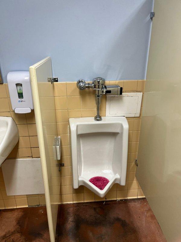 Responded to commercial facility for reported clogged urinal in restroom. Upon arrival, inspected wall-mounted porcelain urinal and chrome flush valve assembly. Diagnosed blockage in urinal drain line causing improper drainage. Utilized drain auger to clear obstruction from urinal trap and waste line. Tested flush valve operation and verified proper water flow and drainage after clearing blockage. Urinal restored to full working condition with no further drainage issues observed.