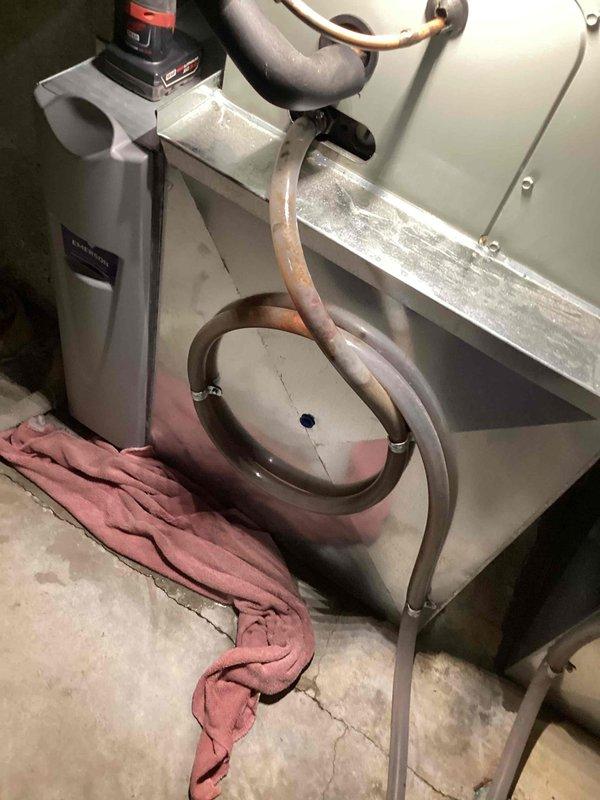 Responded to callback for water leakage issue around AC unit in basement. Upon arrival, found condensate drain line completely clogged, causing water to overflow from drain pan onto floor. Removed heavily corroded drain fitting that had deteriorated and was restricting water flow. Cleared blockage from condensate line, replaced damaged coupling, and tested system operation. Verified proper drainage with no leaks present. Unit cooling normally with condensate now draining properly through repaired line.