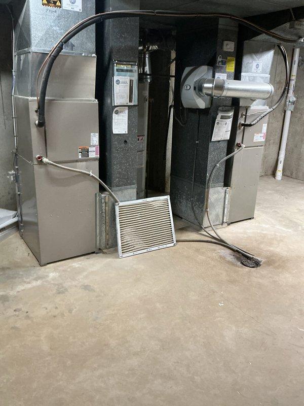 Responded to no cool complaint on 2-zone system with 10+ year old equipment. Upon arrival, performed diagnostic inspection of indoor air handler and outdoor condenser unit. Inspected air filter at indoor unit which showed restriction, checked system operation and airflow. Evaluated outdoor condenser unit condition including fan operation, refrigerant lines, and overall system performance. Documented equipment condition with photos showing both indoor furnace/air handler combination unit in mechanical room and outdoor condensing unit on gravel pad. System assessed for proper cooling operation across both zones.