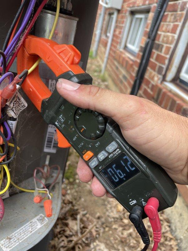 Responded to no cooling call on U10 unit located at side of home with reported issue of system shutting off after running for a period of time. Upon arrival, performed diagnostic testing using clamp meter and measured electrical readings at 6.12 amps. Inspection revealed dirty and neglected unit with significant cobweb accumulation throughout interior compartment and around wire bundles. Removed access panel and inspected internal components including capacitor, wiring connections, and electrical terminals. Found multiple colored wires (purple, red, yellow, black, and green) with poor routing and tangling present. Unit showed signs of extended operation without regular maintenance based on dust and debris buildup on various surfaces and components. Took amp readings on system to assess compressor and electrical component performance. Documented unit condition with photos showing clamp meter readings and interior component layout for service records and customer review.