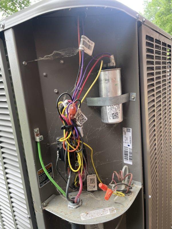 Responded to no cooling call on U10 unit located at side of home with reported issue of system shutting off after running for a period of time. Upon arrival, performed diagnostic testing using clamp meter and measured electrical readings at 6.12 amps. Inspection revealed dirty and neglected unit with significant cobweb accumulation throughout interior compartment and around wire bundles. Removed access panel and inspected internal components including capacitor, wiring connections, and electrical terminals. Found multiple colored wires (purple, red, yellow, black, and green) with poor routing and tangling present. Unit showed signs of extended operation without regular maintenance based on dust and debris buildup on various surfaces and components. Took amp readings on system to assess compressor and electrical component performance. Documented unit condition with photos showing clamp meter readings and interior component layout for service records and customer review.