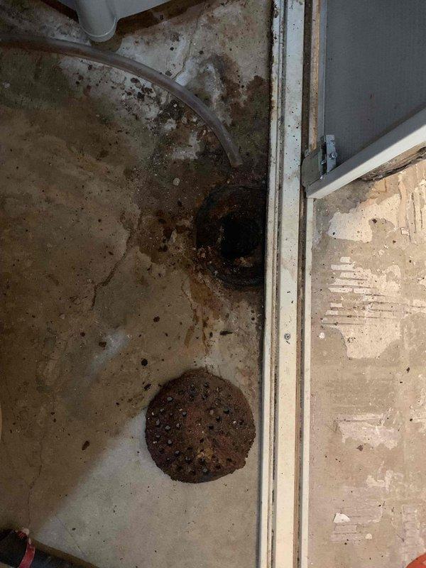 Responded to basement drain concerns regarding possible clogging and drain plate replacement. Upon arrival, found floor drain area with significant water staining, debris accumulation, and biological growth indicating chronic moisture issues. Assessed existing circular perforated drain cover showing heavy rust discoloration and sediment buildup around perimeter and opening. Cleared drain line obstruction and removed accumulated debris from drain assembly. Evaluated floor drain cover condition and surrounding concrete surface deterioration caused by prolonged water exposure. Recommended addressing underlying moisture infiltration to prevent future biological growth and continued floor deterioration.