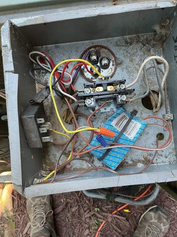 Responded to no cooling call on single residential AC unit located at side of home. Upon arrival, performed system diagnostics and inspection of outdoor condensing unit. Removed electrical disconnect cover to inspect wiring connections and found weathered disconnect box with rust staining throughout interior surfaces. Verified all wire connections at disconnect switch including red, yellow, white, and brown conductors were secure to terminal blocks. Inspected dual capacitors mounted in disconnect enclosure showing signs of age and outdoor exposure.

Accessed interior of condensing unit housing and inspected evaporator coil, refrigerant lines, compressor wiring, and electrical components. Located blue capacitor and associated wiring harness within unit. Examined heat exchanger coil fins for debris accumulation and airflow restrictions. Checked refrigerant line connections and U-bend copper tubing at coil interface. Verified all internal wire routing including red, white, and brown condu
