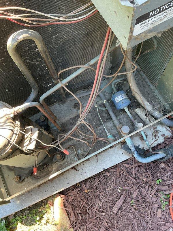 Responded to no cooling call on single residential AC unit located at side of home. Upon arrival, performed system diagnostics and inspection of outdoor condensing unit. Removed electrical disconnect cover to inspect wiring connections and found weathered disconnect box with rust staining throughout interior surfaces. Verified all wire connections at disconnect switch including red, yellow, white, and brown conductors were secure to terminal blocks. Inspected dual capacitors mounted in disconnect enclosure showing signs of age and outdoor exposure.

Accessed interior of condensing unit housing and inspected evaporator coil, refrigerant lines, compressor wiring, and electrical components. Located blue capacitor and associated wiring harness within unit. Examined heat exchanger coil fins for debris accumulation and airflow restrictions. Checked refrigerant line connections and U-bend copper tubing at coil interface. Verified all internal wire routing including red, white, and brown condu