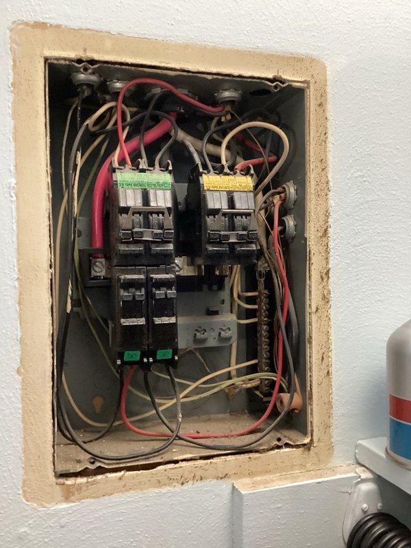 Performed on-site evaluation of existing electrical panel and contactor assembly located in kitchen/living room area. Panel inspection revealed significant age-related deterioration including corrosion, discoloration, and accumulated debris throughout the metal enclosure. Two electrical contactors with multiple wire connections were assessed for condition and functionality. Documented extensive wear on panel enclosure with paint chipping, bare metal exposure at mounting points, and environmental degradation of internal components. Photographed installation to provide comprehensive visual documentation for replacement estimate. Homeowner approval required before proceeding with any recommended repairs or panel upgrade work.
