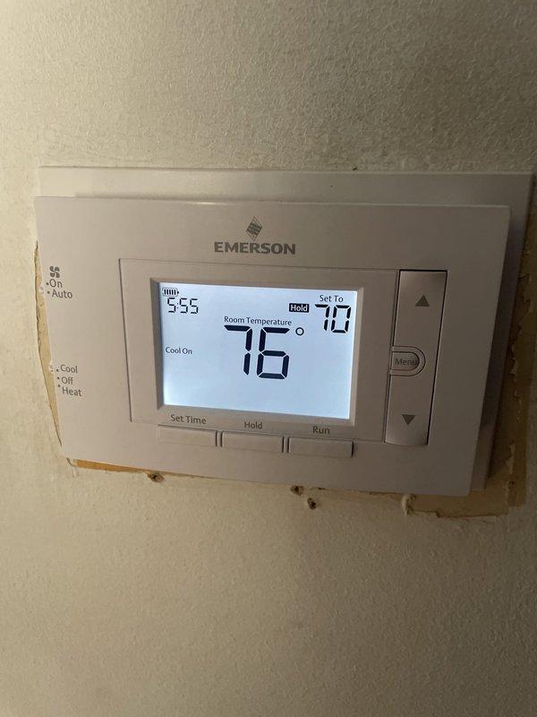 Responded to no cooling complaint on recently installed 2025 unit located in side yard. Upon arrival, found outdoor unit off with only fan running. Verified thermostat operation showing system attempting to cycle but failing to maintain cooling mode. Adjusted thermostat settings from OFF to COOL mode with setpoint at 70°F, confirmed system successfully engaged and began cooling cycle with display indicating "Cool On" at 76°F room temperature. Unit now operating properly and maintaining desired temperature.