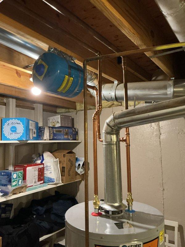 Completed installation of 50-gallon tall gas water heater in basement utility area. Connected unit to existing copper supply lines with brass shut-off valves, installed expansion tank with proper mounting and strapping to ceiling joists, and connected to galvanized flue ductwork. Applied required plumbing identification sticker and verified all connections for proper operation per permit requirements.