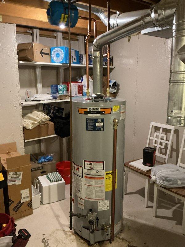 Completed installation of 50-gallon tall gas water heater in basement utility area. Connected unit to existing copper supply lines with brass shut-off valves, installed expansion tank with proper mounting and strapping to ceiling joists, and connected to galvanized flue ductwork. Applied required plumbing identification sticker and verified all connections for proper operation per permit requirements.
