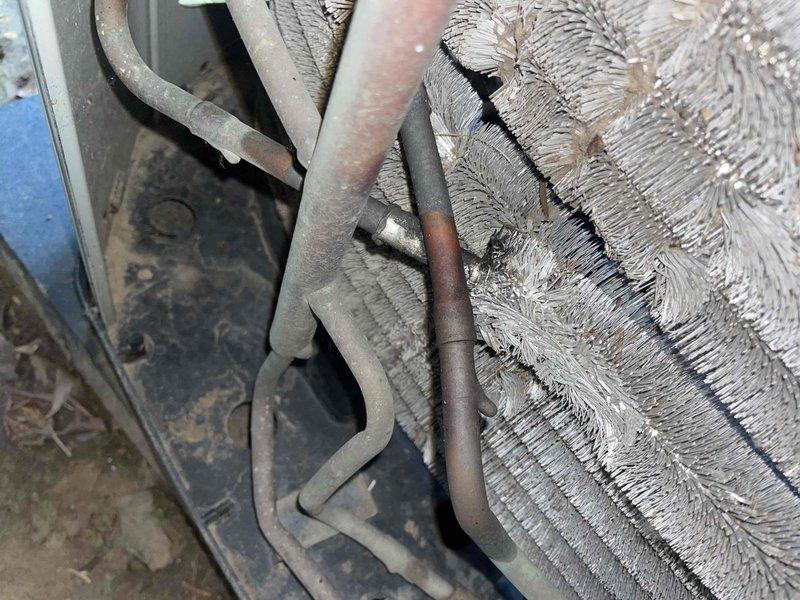 Responded to no cooling complaint on 15-year-old ground-level unit that had received maintenance service days prior. Upon inspection, discovered extensive ice formation on evaporator coil and refrigerant lines, indicating restricted airflow rather than low refrigerant charge. Found evaporator coil heavily contaminated with dust and debris buildup between fins, preventing adequate air circulation across heat exchanger. Documented frozen coil conditions with significant frost crystallization on copper suction line and coil surfaces. System shut down to allow complete ice melt before further diagnosis. Identified restricted airflow as root cause of warm air complaint, requiring coil cleaning and possible blower motor evaluation to restore proper system operation.
