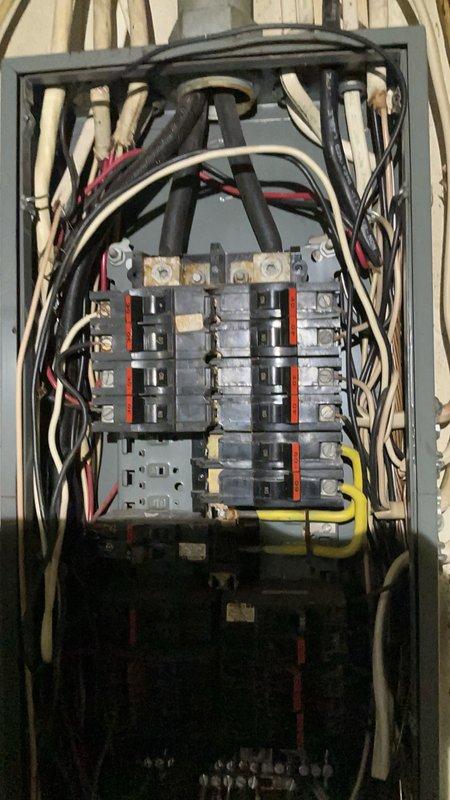 Responded to service call for electrical panel with water intrusion. Upon arrival, found 12-4 panel box completely flooded with water, creating immediate safety hazard and potential for electrical failure. Documented existing conditions showing disorganized wiring with multiple colored conductors (black, white, red, yellow) entering through top of gray metal enclosure mounted on wooden wall. Panel contained multiple circuit breakers in various configurations with orange/red bus bars running vertically for power distribution. Performed necessary remediation to address water damage and restore safe electrical service to the panel installation.