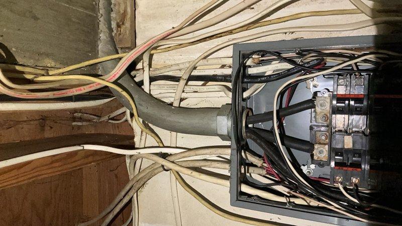 Responded to service call for electrical panel with water intrusion. Upon arrival, found 12-4 panel box completely flooded with water, creating immediate safety hazard and potential for electrical failure. Documented existing conditions showing disorganized wiring with multiple colored conductors (black, white, red, yellow) entering through top of gray metal enclosure mounted on wooden wall. Panel contained multiple circuit breakers in various configurations with orange/red bus bars running vertically for power distribution. Performed necessary remediation to address water damage and restore safe electrical service to the panel installation.