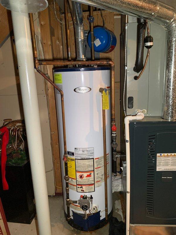 Responded to service call for reported AC unit leaking in basement. Upon arrival, discovered water accumulation on concrete floor around HVAC system area. Investigation revealed the moisture was originating from the water heater rather than the air conditioning unit. Observed active water staining and pooling at the base of the 10-year-old residential water heater, with towels placed to absorb leakage. Inspected water heater connections, copper piping, pressure relief valve, and base assembly for source of leak. Documented conditions with photographs showing water damage on floor and component configuration. Identified leak issue requiring repair and provided customer with findings and repair recommendations for the water heater.