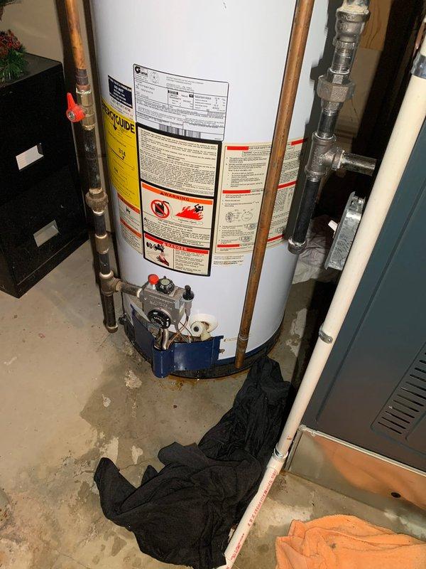Responded to service call for reported AC unit leaking in basement. Upon arrival, discovered water accumulation on concrete floor around HVAC system area. Investigation revealed the moisture was originating from the water heater rather than the air conditioning unit. Observed active water staining and pooling at the base of the 10-year-old residential water heater, with towels placed to absorb leakage. Inspected water heater connections, copper piping, pressure relief valve, and base assembly for source of leak. Documented conditions with photographs showing water damage on floor and component configuration. Identified leak issue requiring repair and provided customer with findings and repair recommendations for the water heater.