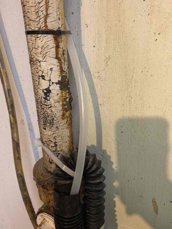 Responded to a recall for kitchen sink drainage issues and washing machine leak that occurred following previous plumbing service. Upon arrival, inspected kitchen sink drainage system and washing machine area in 80-year-old home. Documented severely deteriorated vertical drain pipe with extensive surface degradation and peeling, along with aging flexible hoses and connections in utility area. Assessed plumbing infrastructure showing significant wear consistent with building age, including compromised pipe coatings and outdated drainage components that required attention to resolve both the dual-basin sink stoppage and washing machine leak concerns.