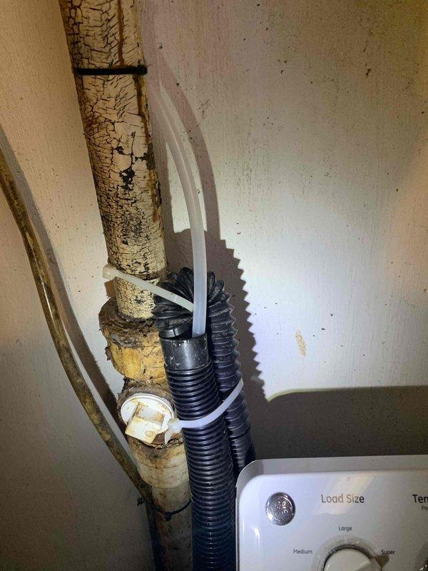 Responded to a recall for kitchen sink drainage issues and washing machine leak that occurred following previous plumbing service. Upon arrival, inspected kitchen sink drainage system and washing machine area in 80-year-old home. Documented severely deteriorated vertical drain pipe with extensive surface degradation and peeling, along with aging flexible hoses and connections in utility area. Assessed plumbing infrastructure showing significant wear consistent with building age, including compromised pipe coatings and outdated drainage components that required attention to resolve both the dual-basin sink stoppage and washing machine leak concerns.