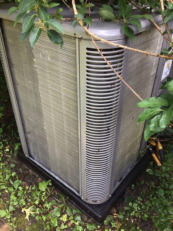 Responded to no-cooling complaint on residential air conditioning system less than 10 years old located in backyard. Upon arrival, found outdoor condenser unit significantly obstructed by overgrown vegetation including vines, branches, and dense foliage covering top and sides of equipment, restricting proper airflow to coil and fan assembly. Advised customer to turn unit off and operate in fan-only mode to prevent compressor damage. Cleared vegetation from around condenser to restore adequate clearance for airflow and heat rejection. Inspected unit for additional issues related to warm air discharge complaint. Documented equipment condition with photographs showing vegetation obstruction and weathered exterior panels. Recommended ongoing vegetation management to maintain minimum clearance requirements for optimal system performance and efficiency.