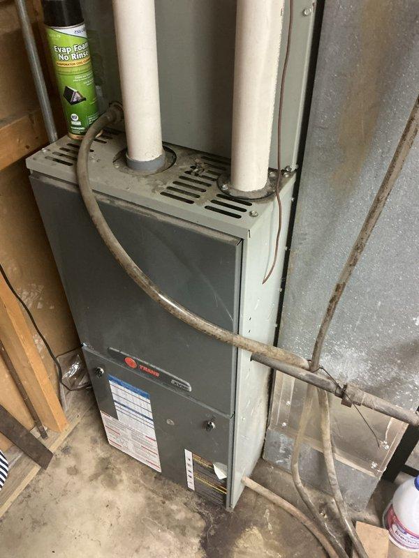 Responded to no cooling complaint affecting entire residence with 18-year-old Trane system. Upon arrival, performed comprehensive diagnostic evaluation of both indoor and outdoor equipment. Inspected indoor furnace/air handler unit and accessed control board compartment to examine electrical connections and circuit boards. Documented system age and overall condition through visual inspection of equipment, noting multiple control boards, wiring harnesses, and internal components. Photographed furnace installation showing PVC venting configuration and ductwork connections, as well as internal electrical components including dual green circuit boards and wire routing. Given the advanced age of the system (17-20 years old) and no cooling condition, provided customer with assessment findings and recommended next steps for system evaluation and repair options to restore cooling function to the home.