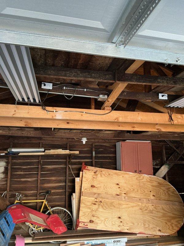 Completed electrical estimate for garage fixture installation in attic space with exposed structural framework. Assessment included evaluation of existing fluorescent lighting, conduit routing along wooden beams, junction box placement, and determination of materials required for fixture upgrades. Documented current wiring configuration and structural mounting points for fixture installation planning.