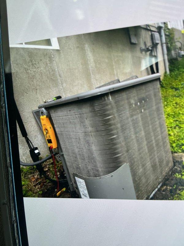 Responded to service call for 15-year-old air conditioning system experiencing intermittent clicking noise from outdoor condenser unit. Upon arrival, performed comprehensive inspection of exterior unit and found system still operational and providing adequate cooling despite audible concern. Conducted thorough cleaning of condenser coils which showed significant accumulation of debris, organic matter, and weathering consistent with unit age and outdoor exposure. Removed leaves and debris from base of unit and surrounding area. Inspected electrical disconnect box, wiring connections, and conduit for any loose components that could contribute to clicking sounds. Documented unit condition with photographs showing exterior weathering, organic growth on casing, and general maintenance needs. System tested and confirmed operational following service completion.