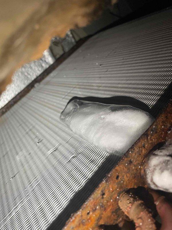 Responded to no-cool service call for single outdoor unit system over 10 years old struggling to maintain 69-degree setpoint with indoor temperature at 76 degrees. Upon inspection, discovered extensive ice buildup on evaporator coil with restricted airflow through aluminum fins. Documented frozen coil condition and observed significant corrosion on drain pan and housing components indicating long-term moisture exposure issues. Advised customer to turn AC off and leave fan on to allow coil to thaw completely. System requires further diagnosis after thaw cycle to determine root cause of freezing condition, which may include low refrigerant charge, restricted airflow from dirty filter or blower issues, or failing metering device.
