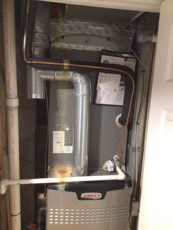 Responded to no-cool call with water dripping from ceiling near indoor air handler on Lennox system installed December 2022. Upon inspection, discovered condensate drainage issue causing water overflow from the air handler unit. Found evidence of water staining on insulation material surrounding ductwork penetration through wall cavity, indicating active leak when system operates. Inspected condensate drain line routing and PVC drainage system for blockages or improper pitch. Verified air handler cabinet installation and condensate pan condition. Documented system configuration including furnace, ductwork connections, and copper refrigerant line routing. Photographed affected areas showing water damage patterns on insulation and mechanical space layout for warranty documentation purposes. System evaluated for proper drainage function to prevent further ceiling water intrusion during cooling operation.