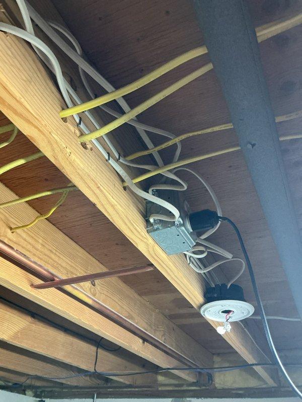 Completed comprehensive electrical inspection of residential property focusing on exposed wiring systems in attic space and HVAC electrical connections. Inspected bundled yellow electrical cables and white communication wiring running along structural beams, verified proper mounting of junction boxes and cylindrical fixtures, and examined conduit installations. Evaluated internal electrical components of wall-mounted HVAC unit, including motor housing, control wiring, and connection integrity. All systems found to be properly installed and functioning within normal parameters.