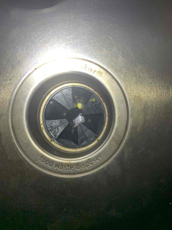 Responded to kitchen sink backup issue. Upon arrival, inspected the garbage disposal unit and drain assembly. Found significant accumulation of food waste debris and yellowish-green residue buildup on the disposal's impeller blades and grinding components. The rubber baffle showed signs of debris accumulation, and the disposal grinding chamber exhibited tarnishing and deposits that were restricting proper drainage and disposal function. Cleared the obstruction, removed debris from the impeller assembly, and restored proper drainage flow to the kitchen sink.