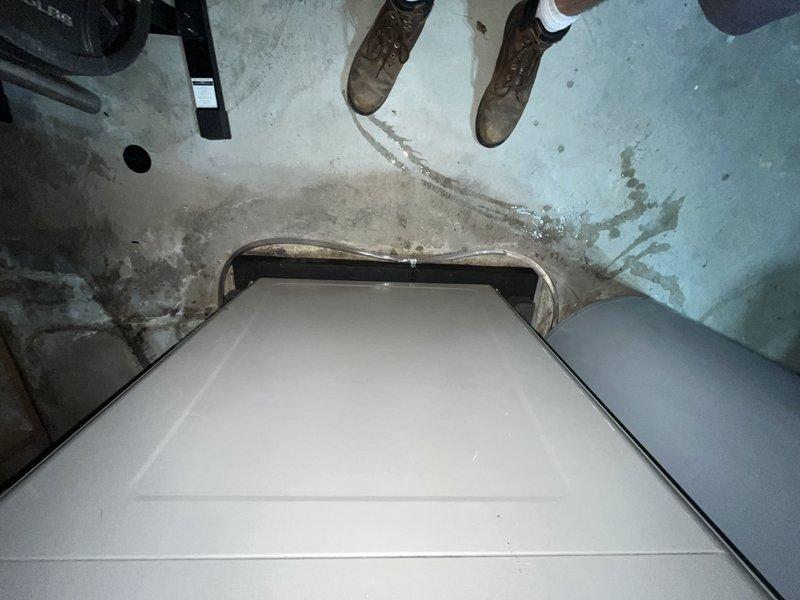 Responded to no cooling complaint on 14-year-old GeoComfort geothermal heat pump system. Upon arrival, confirmed air handler was operating and circulating air through ductwork, but system was not producing cool air. Performed diagnostic evaluation of ground source heat pump components. Inspected air handler unit located in mechanical room, checked refrigerant lines, and verified electrical connections. Documented equipment condition and installation environment showing age-related wear in utility space. System evaluation revealed cooling malfunction requiring further assessment of compressor operation and refrigerant circuit. Photographed equipment for service records showing air handler cabinet and copper refrigerant line connections in basement installation area with visible moisture exposure patterns on surrounding surfaces.