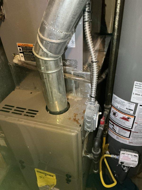 Responded to emergency water leak call with AC system flooding above downstairs furnace. Upon arrival, found excessive condensate water accumulation requiring towel changes every one to two hours. Inspected 10-year-old ground-level outdoor unit and traced source to condensate drainage issue in attic ductwork and plenum area. Examined HVAC system components including air handler, ductwork connections, and condensate drain lines. Identified blockage or improper drainage causing water overflow from drain pan. Cleared condensate line obstruction and verified proper drainage flow. Inspected surrounding areas including water heater and furnace for any secondary water damage or related issues. Tested system operation to ensure condensate removal functioning correctly and no further leaking present. Documented equipment conditions and repair work with photographs of attic plenum assembly and utility area showing furnace and adjacent equipment.