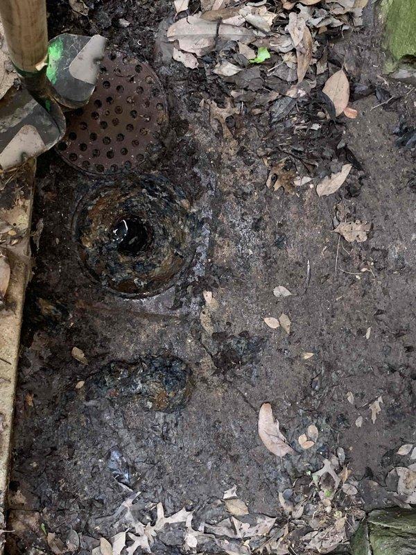 Performed video camera inspection of main sewer line to investigate reported backup issues at rear drain. Camera inspection revealed significant deterioration and corrosion of pipe interior at approximately 64 feet 9 inches from access point, with visible mineral deposits, scaling, and compromised pipe integrity. Documented conditions including standing water, corroded metal surfaces, and structural degradation throughout the affected section. Captured photographic evidence of exterior access point and internal pipe conditions for further evaluation and follow-up repair recommendations.