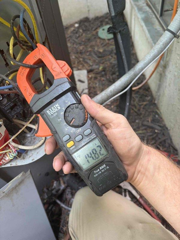 Completed preventive maintenance tune-up on residential split system air conditioning unit with outdoor condenser located on ground-level concrete pad. Performed comprehensive system inspection including visual examination of condenser cabinet, coil fins, and electrical components. Verified proper electrical operation with amperage readings showing 48.2 amps at compressor circuit using clamp meter. Inspected disconnect box and electrical connections for secure terminations and proper wire routing. Cleaned debris including organic material from base of unit and surrounding area. Confirmed condenser fan operation, adequate clearances from structure, and overall system functionality. Unit operating within normal parameters upon completion of tune-up service.
