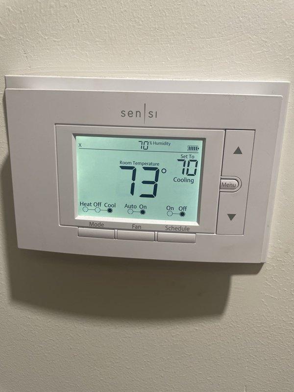 Responded to report of draft sound coming from furnace unit. Upon arrival, performed system diagnostic on residential HVAC unit located in side yard, less than 10 years old. Inspected Sensi digital thermostat showing 73°F ambient temperature with cooling mode set to 70°F and 70% humidity reading. Evaluated air filtration system and identified need for filter maintenance. Provided customer with replacement air filters and documented equipment condition through photographs. System operational at time of departure.