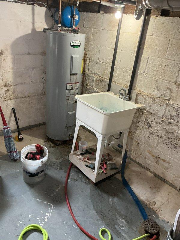 Completed installation of a 50-gallon STERLING electric tall water heater in basement utility area. Unit installed with proper copper piping connections, blue expansion tank mounted above, and all connections secured to code. Permit #26PLU-14749 applied with required plumbing identification sticker affixed to unit for inspection compliance.