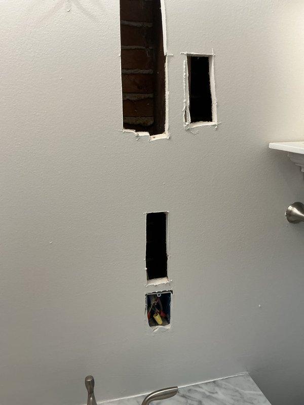 Completed electrical estimate and assessment for multiple fixture and outlet issues throughout the residence. Evaluated bathroom renovation requiring new outlet installation with visible wall openings prepared for electrical work. Inspected basement area with exposed hanging wires requiring proper termination and securing. Assessed non-functional outdoor lighting fixture and determined repair requirements. Examined garage space lacking electrical infrastructure for both outlet and lighting installation. Evaluated malfunctioning stairwell light fixture at upper landing. Identified four three-pronged outlets throughout the property that lack proper grounding and require remediation to meet current electrical code standards. Documented all conditions with photographic evidence showing bathroom wall penetrations with exposed wiring ready for fixture installation.