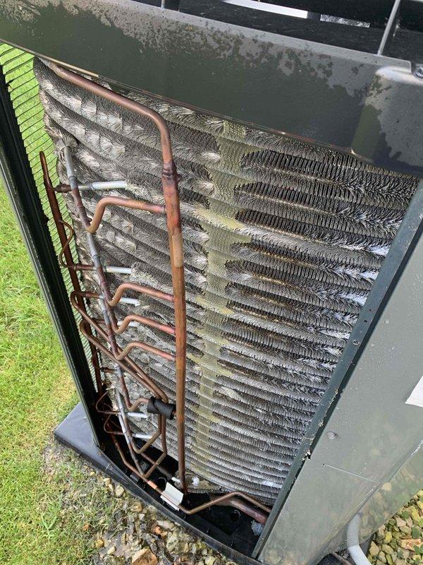 Responded to emergency no-cool call for 2019 Trane system unable to maintain temperature below 77°F. Upon inspection, found condenser coil heavily obstructed with dirt, debris, and organic material buildup significantly restricting airflow through fins. Removed side panel and documented severe contamination on condenser coil assembly. Performed thorough coil cleaning to remove accumulated debris and restore proper airflow. Inspected copper refrigerant lines showing age-related oxidation but no leaks detected. System restored to normal cooling operation following coil cleaning service.